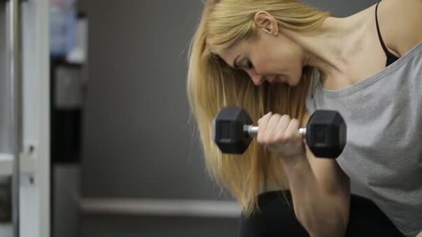 The girl performs an exercise with dumbbells
